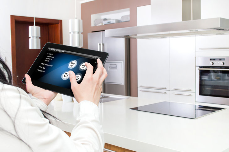 Hvidt moderne køkken, hvor en kvinde styrer teknologien i køkkenet med en tablet.