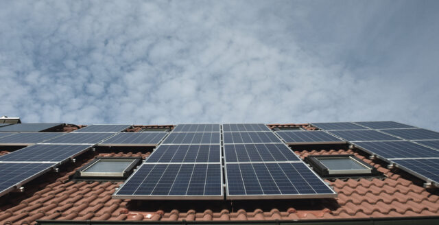 Solceller til sommerhuset på et rødt tag og med en blå himmel i baggrunden.