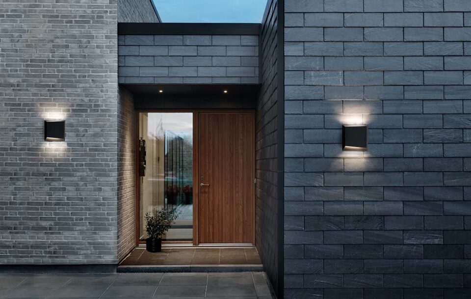 Et hus hvor man grundigt har foretaget et valg af udendørslamper, som lyser murstenene op på huset.